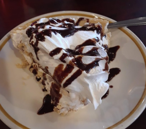 A slice of pie topped with whipped cream and drizzled with chocolate sauce on a white plate.
