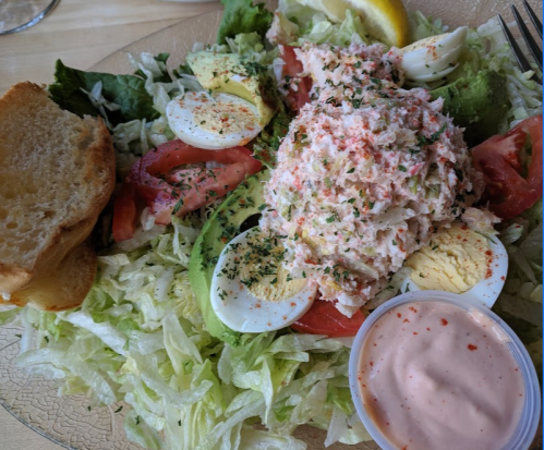 A fresh salad with lettuce, tomatoes, avocado, hard-boiled eggs, crab meat, and a side of dressing, served with bread.