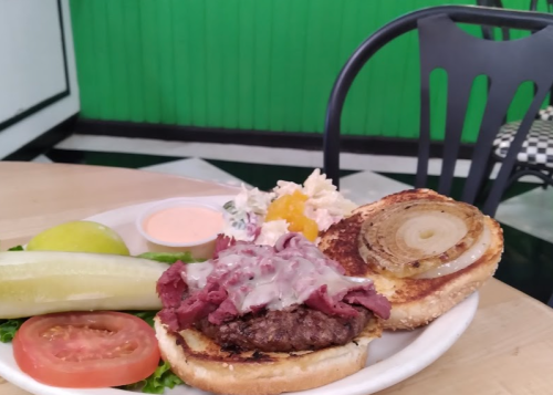 A plate featuring a burger with roast beef, melted cheese, lettuce, tomato, pickles, and a side salad on a table.