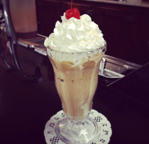 A tall glass filled with a creamy dessert topped with whipped cream and a cherry.