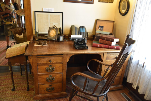 A vintage wooden desk with a typewriter, books, and framed photos, set in a cozy, well-lit room.