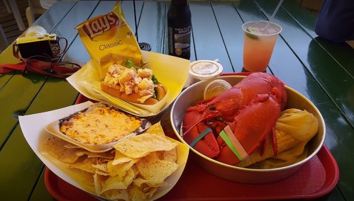 A colorful meal featuring lobster, nachos, a salad, and drinks on a green table.