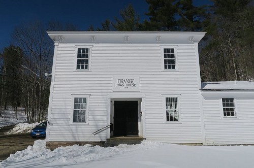White two-story building with "Orange Town House" sign, surrounded by snow and trees under a clear blue sky.