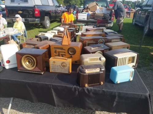 A table displaying various vintage radios in different styles and colors at an outdoor market.