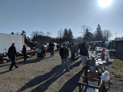 A bustling outdoor flea market with people browsing tables and vendors under a clear blue sky.