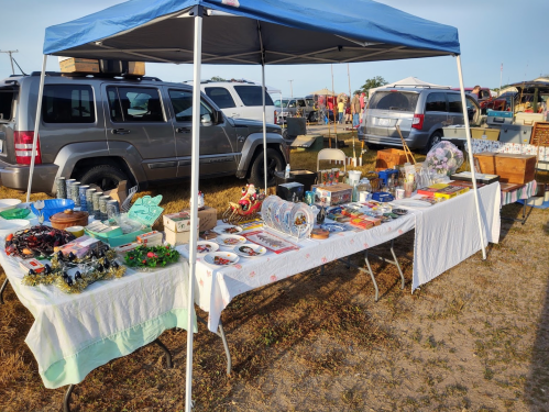 A market stall under a blue canopy displaying various handmade crafts and goods on tables.