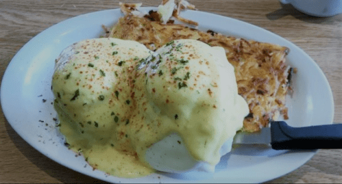 A plate of eggs Benedict topped with hollandaise sauce and a side of crispy hash browns.