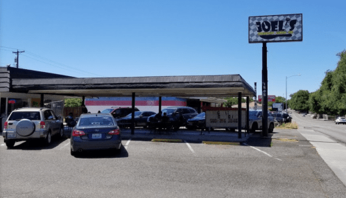 A restaurant named Joel's with a covered outdoor seating area and parked cars on a sunny day.