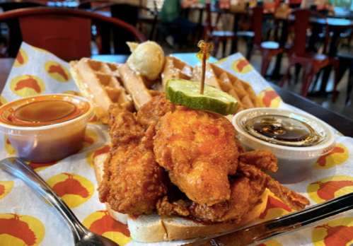 A plate of fried chicken on waffles, garnished with lime and served with dipping sauces, in a casual dining setting.