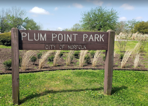 Sign for Plum Point Park in Norfolk, featuring greenery and a clear blue sky in the background.