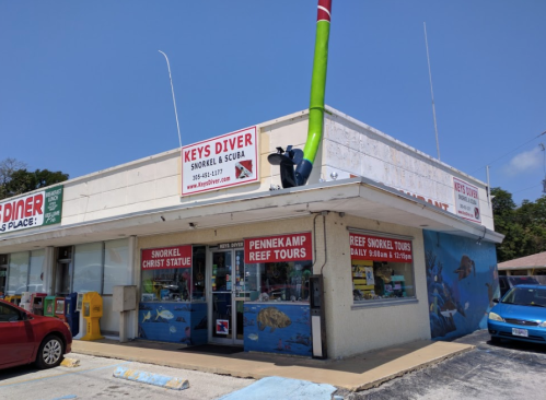 A colorful dive shop with a large green snorkel decoration, featuring signs for snorkeling and reef tours.