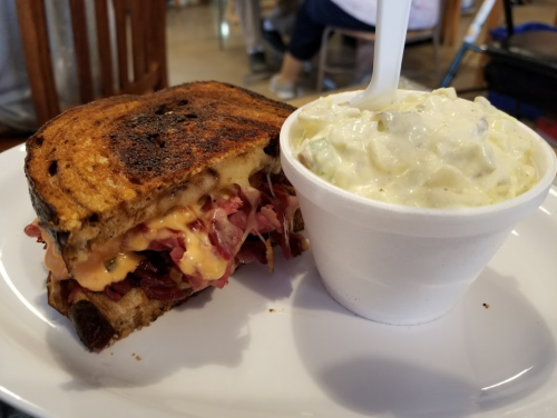 A toasted sandwich filled with melted cheese and meat, served with a side of creamy coleslaw in a cup.