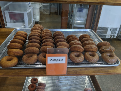 A display of pumpkin donuts on a tray, featuring various styles and toppings, in a bakery setting.