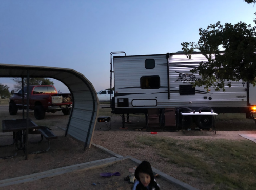 A camper parked at dusk with a red truck nearby and a child playing in the foreground.