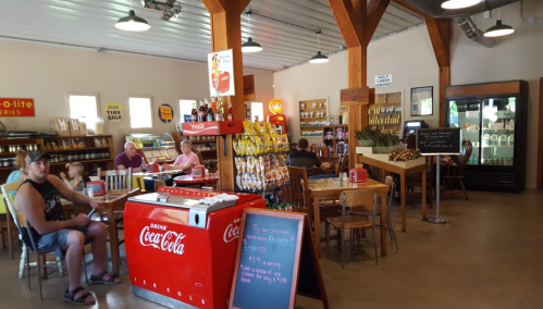 A cozy diner with wooden beams, tables, and a vintage Coca-Cola cooler, featuring patrons enjoying their meals.