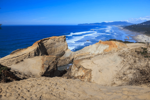 A scenic view of a sandy cliff overlooking a blue ocean and coastline under a clear blue sky.