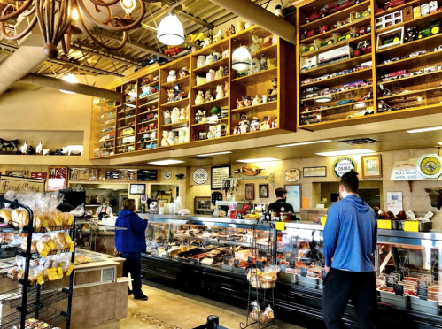 A cozy deli with a display case of meats, shelves filled with collectibles, and customers browsing the offerings.