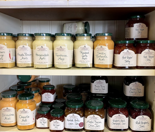 A shelf filled with various jars of sauces, aiolis, jams, and jellies, all labeled with decorative tags.