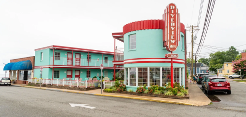 A colorful retro-style motel with a round entrance, featuring turquoise and red accents, located on a quiet street.