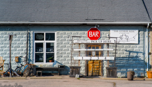 A blue building with a bar sign, pickup area, and a bicycle outside, featuring a rustic, welcoming atmosphere.