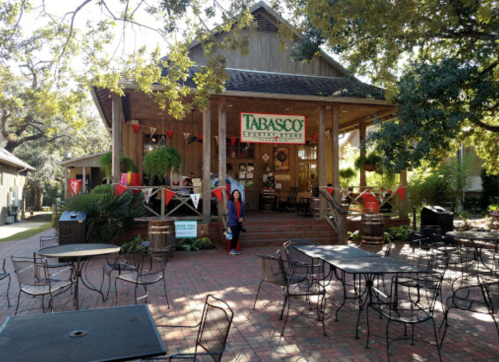 A rustic building with a "Tabasco" sign, surrounded by trees and outdoor seating, in a sunny courtyard.