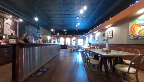 A cozy café interior with wooden tables, a counter, and colorful artwork on the walls, illuminated by soft lighting.