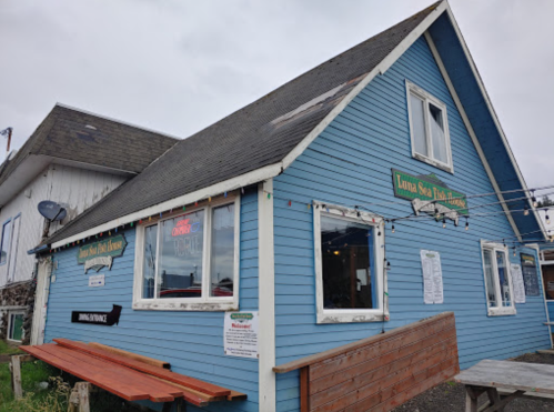 A blue, two-story building with a sloped roof, featuring a sign for "Luna Sea Fish House" and outdoor seating.
