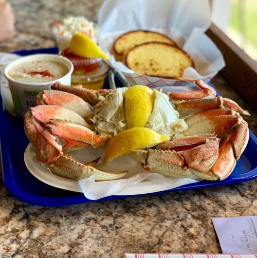 A large crab on a plate with lemon wedges, accompanied by coleslaw, bread, and a cup of soup on a tray.