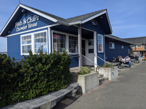 A blue building with a sign reading "Fish & Chips Chowder House," featuring outdoor seating and diners.