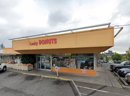 Exterior of Lucky Donuts shop with a bright orange facade and large signage, surrounded by parked cars and greenery.