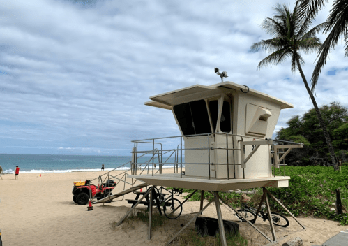 A lifeguard tower on a sandy beach with palm trees, overlooking the ocean and a red ATV nearby.