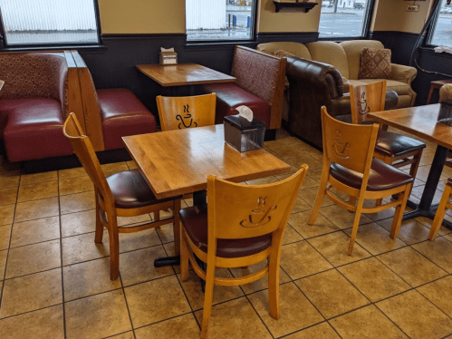 Cozy café interior with wooden tables, chairs, and cushioned seating areas. Warm, inviting atmosphere.