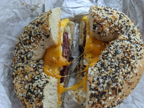 A toasted bagel with sesame and poppy seeds, filled with melted cheese and layers of meat.
