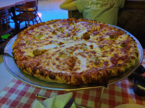 A large, freshly baked pizza with melted cheese and toppings, served on a round metal tray.