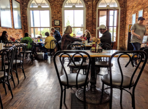 A cozy café with wooden floors, brick walls, and patrons enjoying meals at tables.