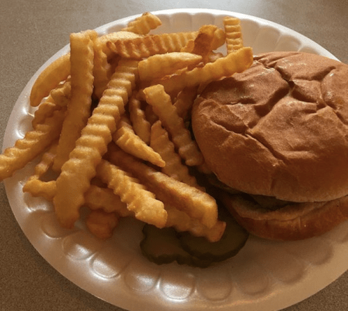 A plate with crinkle-cut fries and a hamburger sandwich, accompanied by a slice of pickle.