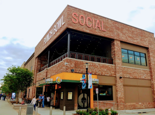 Exterior of Punch Bowl Social, a brick building with large windows and a colorful entrance, on a cloudy day.