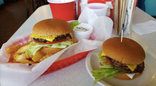 Two burgers with lettuce, tomato, and cheese, served with crinkle-cut fries and a side of coleslaw on a table.