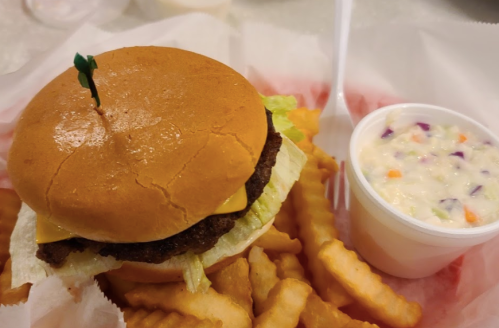 A cheeseburger with lettuce on a bun, served with crinkle-cut fries and a cup of coleslaw.