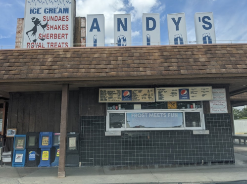 A vintage ice cream stand named Andy's, featuring a menu board and colorful signage under a blue sky.