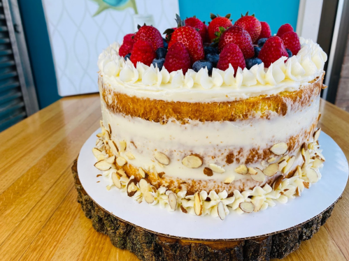 A layered cake topped with strawberries and blueberries, decorated with almond slices on a wooden cake stand.