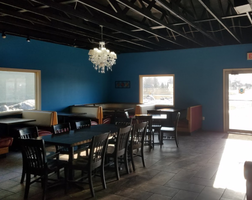 Interior of a restaurant featuring blue walls, a chandelier, and tables with chairs, illuminated by natural light.
