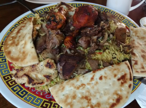 A colorful plate of mixed grilled meats, rice, and flatbreads, garnished with herbs and spices.
