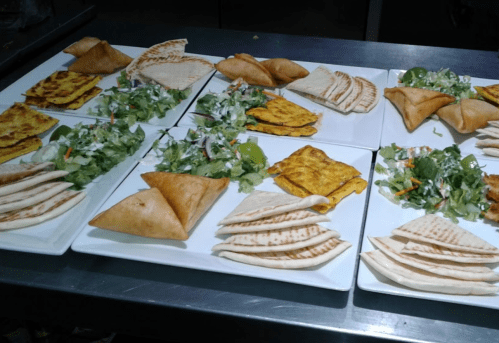 A variety of dishes on white plates, including salads, flatbreads, and stuffed pastries, arranged on a metal surface.