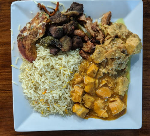 A plate of rice, chicken curry, grilled meat, and sautéed vegetables, served on a white square dish.