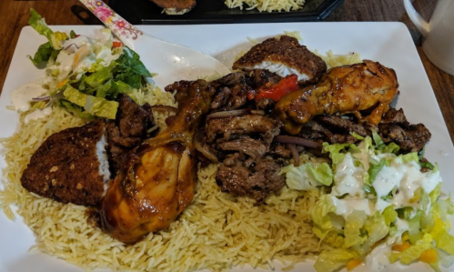 A plate of rice topped with grilled chicken, beef, falafel, and a side salad with dressing.