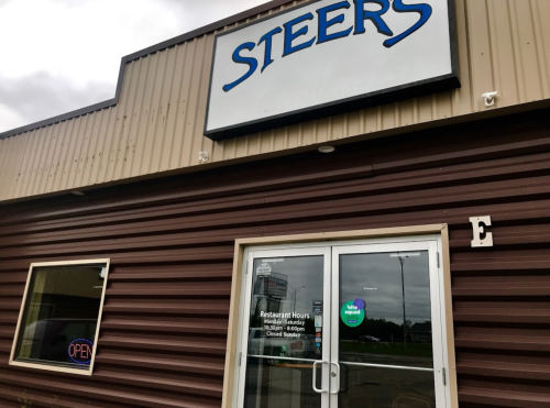 Exterior of a restaurant named "Steers," featuring a glass door with an "Open" sign and visible hours of operation.