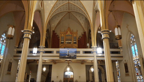 Interior of a church featuring tall arches, stained glass windows, and a large organ above the altar.