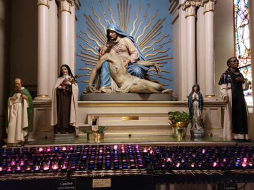 A religious altar featuring a statue of Mary holding Jesus, surrounded by candles and figures of saints.
