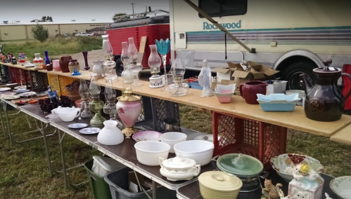 A table filled with various vintage items and glassware, set up outdoors near an RV.
